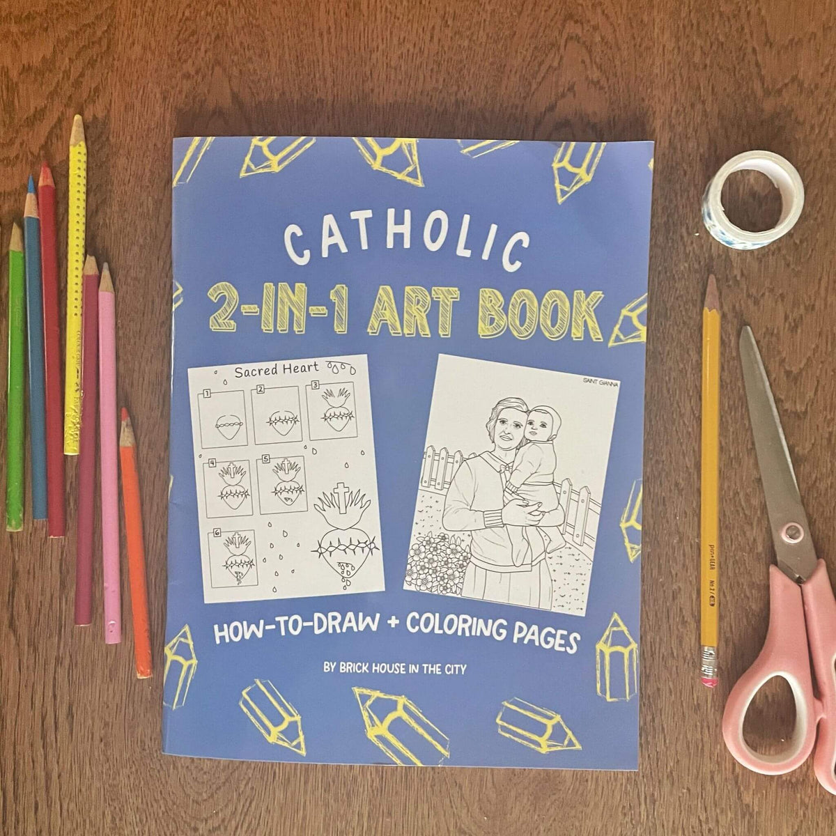 Catholic 2-In-1 Art Book cover with colored pencils, featuring how-to-draw and coloring pages on a wooden table.