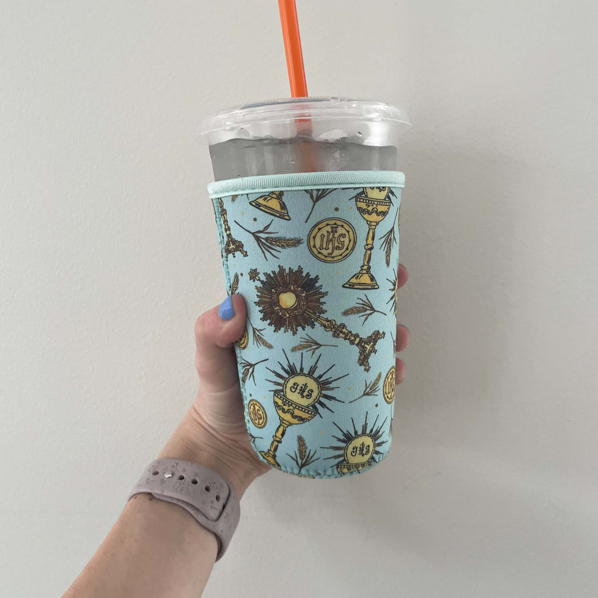 Catholic Cold Cup Sleeve in Eucharistic design, neoprene insulated for cold drinks, shown on a cup with a hand holding it.