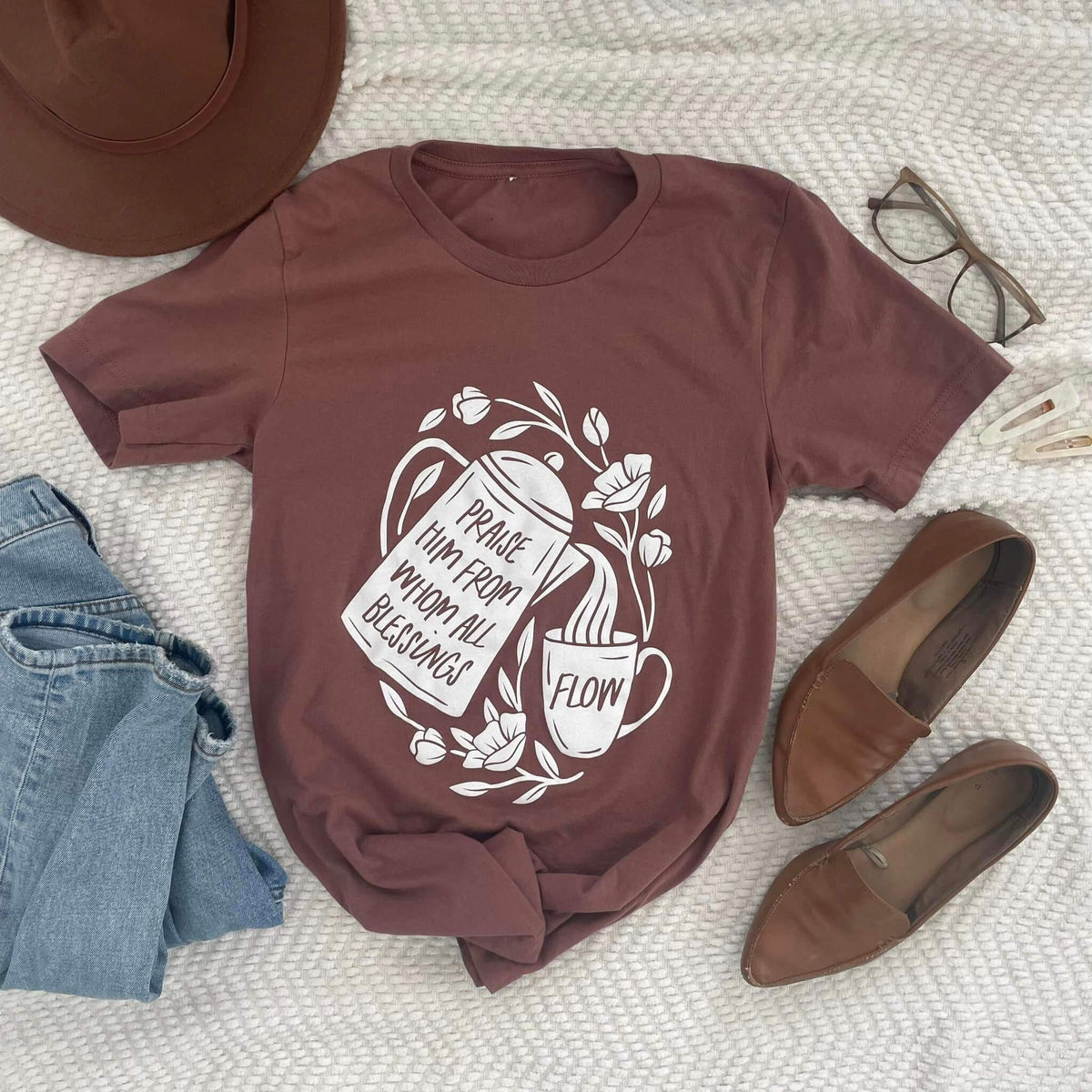 Brown tee with 'Praise Him from whom all blessings flow' design featuring coffee pot pouring into cup, surrounded by flowers.