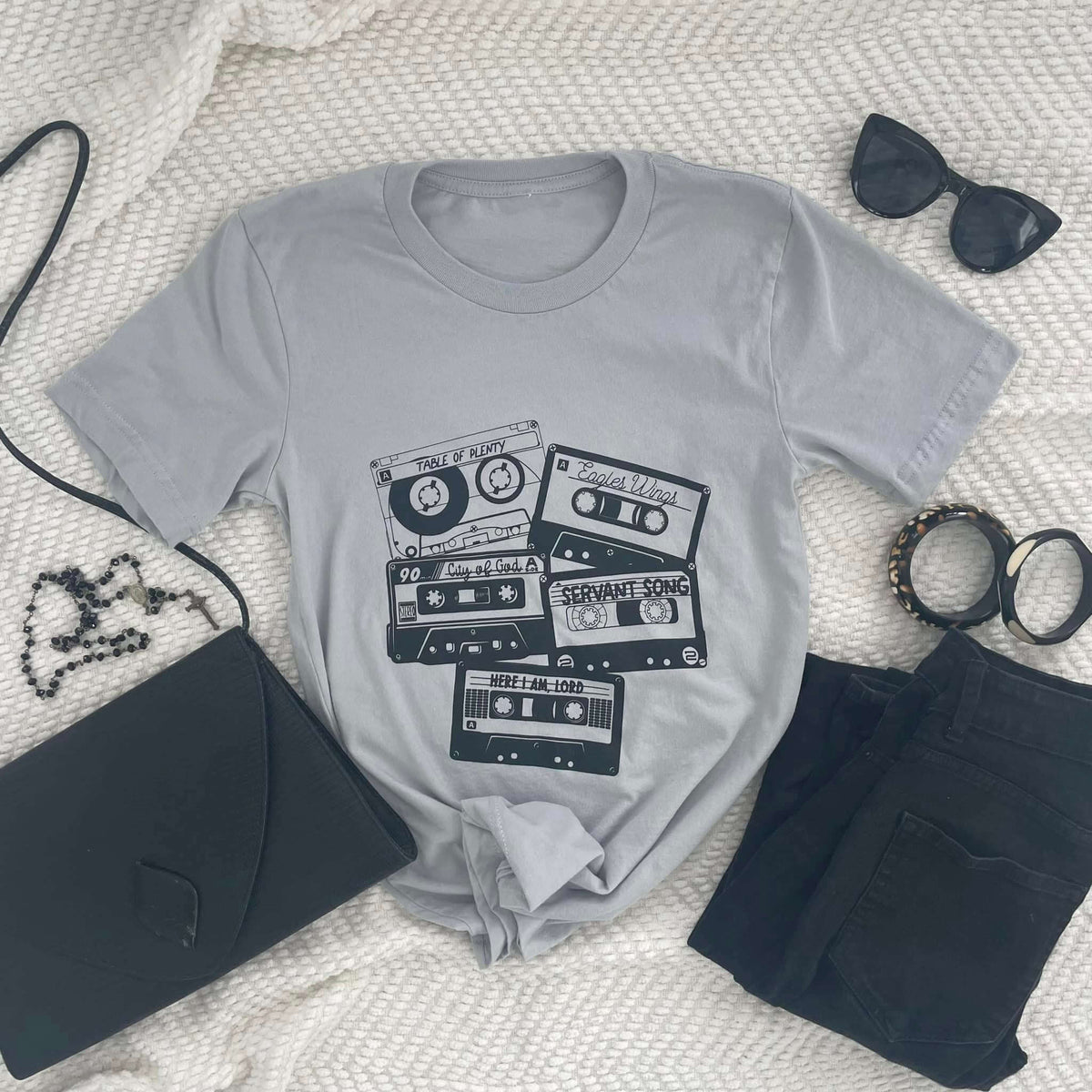 Cassette shirt featuring nostalgic church songs like 'Table of Plenty' and 'Servant Song', styled with accessories on a white background.