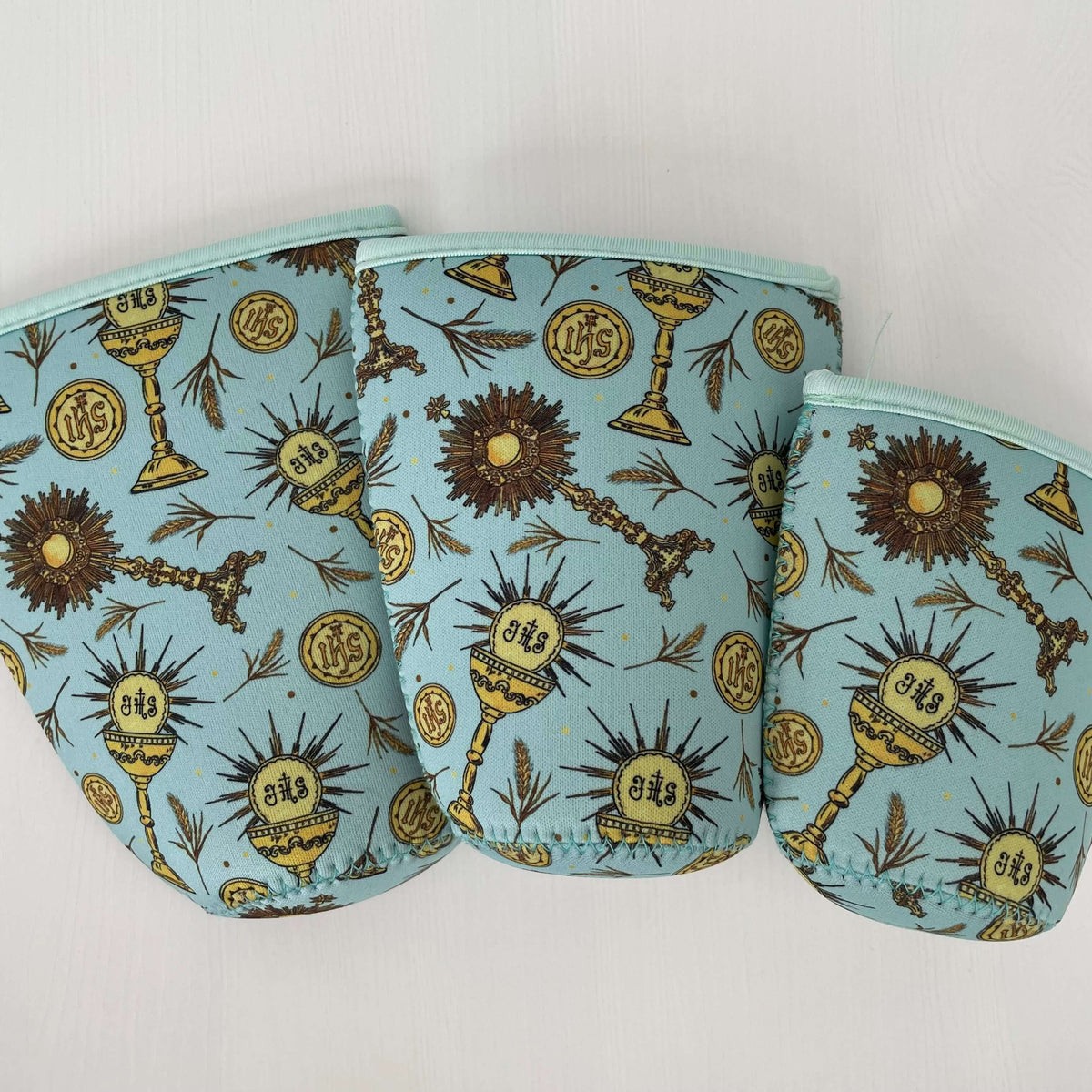 Eucharistic Catholic cold cup sleeves in various sizes with religious motifs on light blue background.