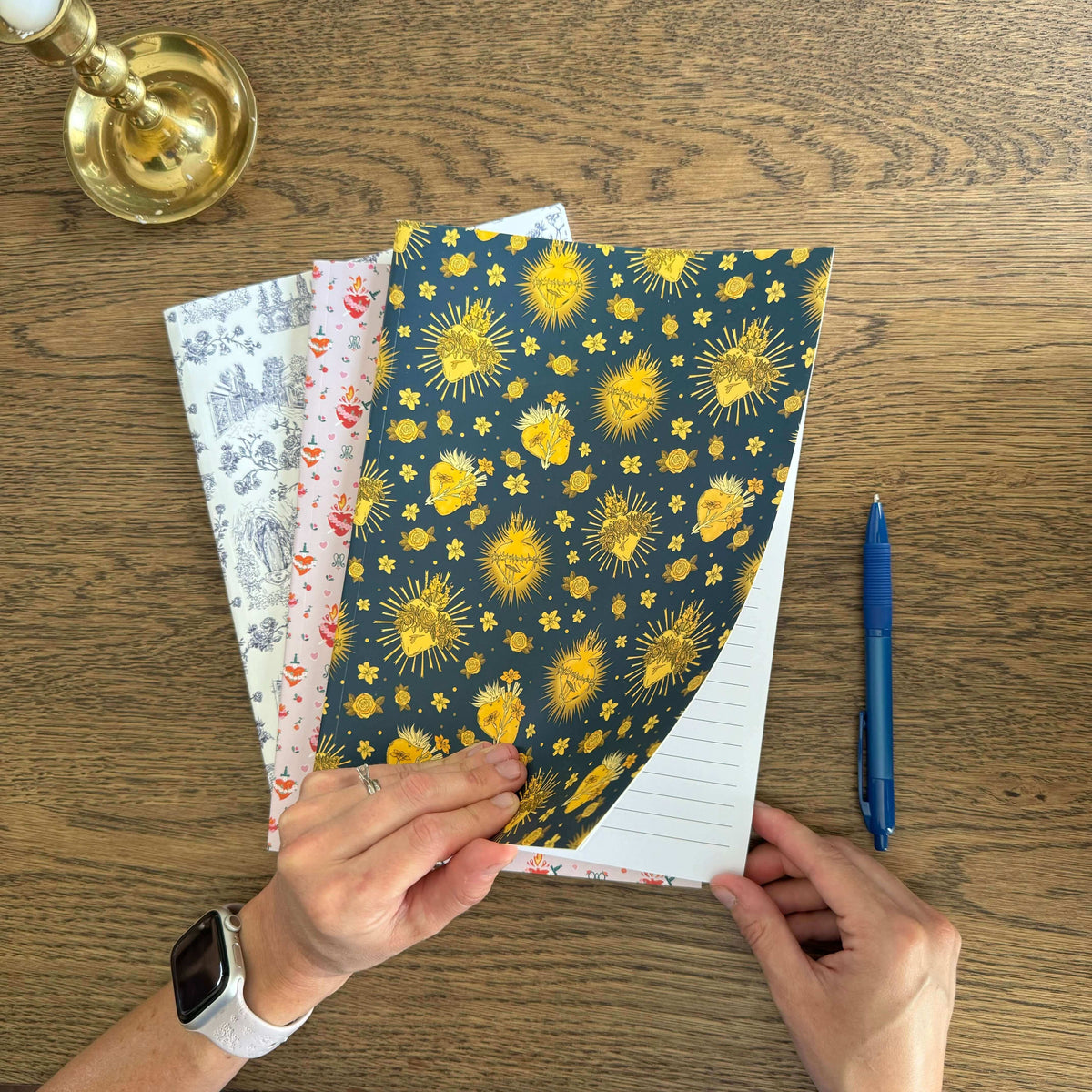 Person holding a collection of Catholic composition notebooks with holy hearts design and pen on wood table.