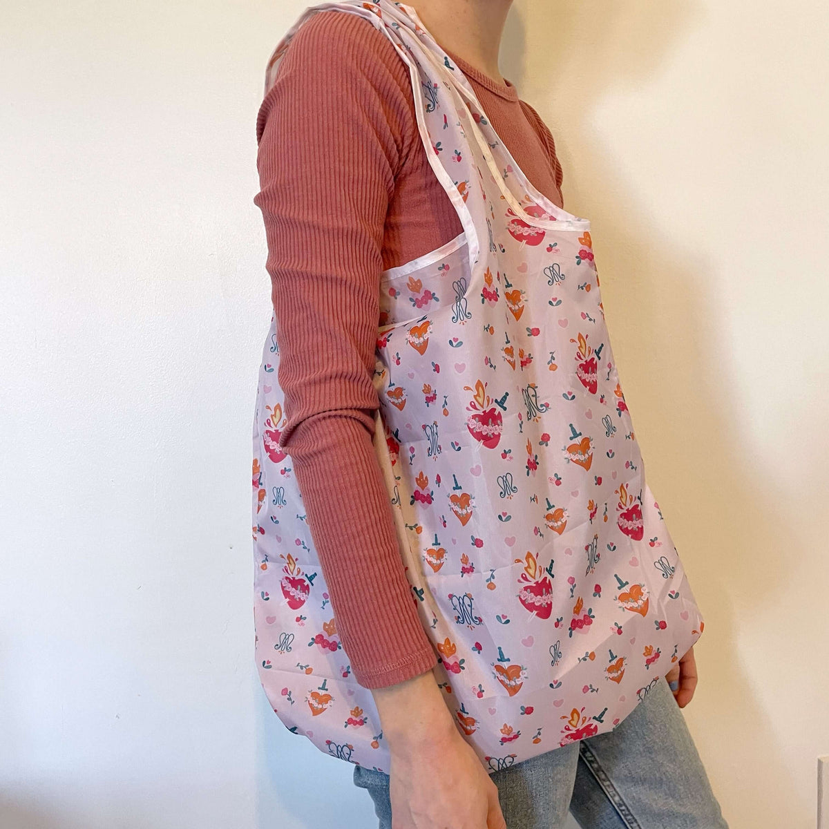 Person carrying a Catholic reusable grocery bag with Auspice Maria pattern, eco-friendly polyester design in pink, 26.5x19 inches.