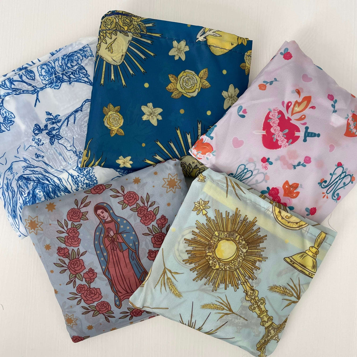 Catholic reusable grocery bags from Mary's Garden Collection featuring religious patterns like Lourdes, Guadalupe, and Holy Hearts.