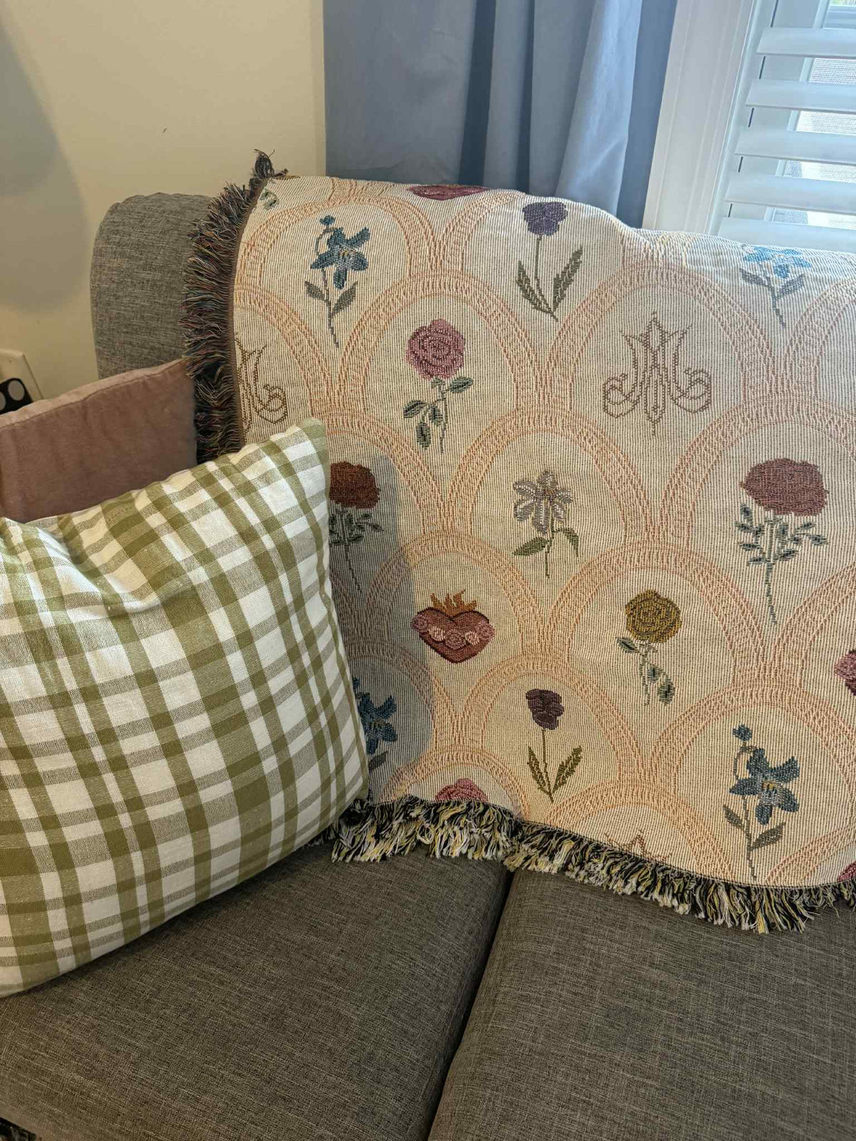 Mary's Sacred Garden Woven Blanket with floral design on a sofa next to a plaid pillow
