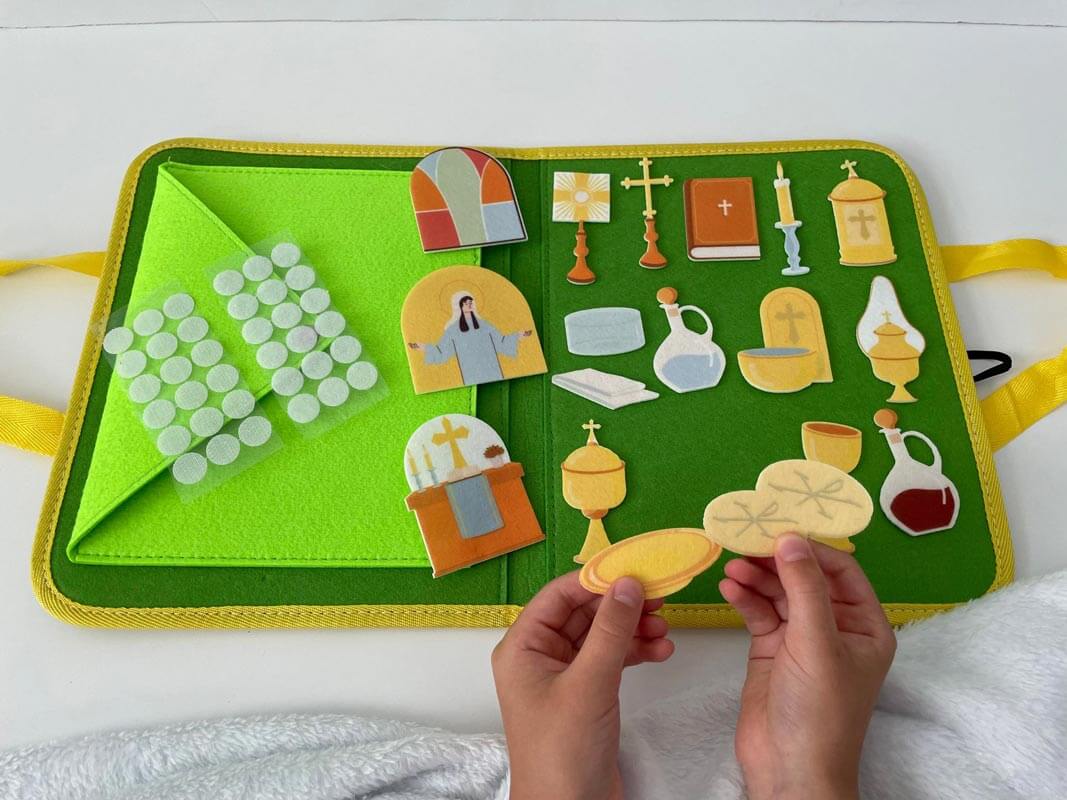 Child playing with Catholic Mass Felt Book Kit featuring church symbols like bread, chalice, and priest on bright green background.