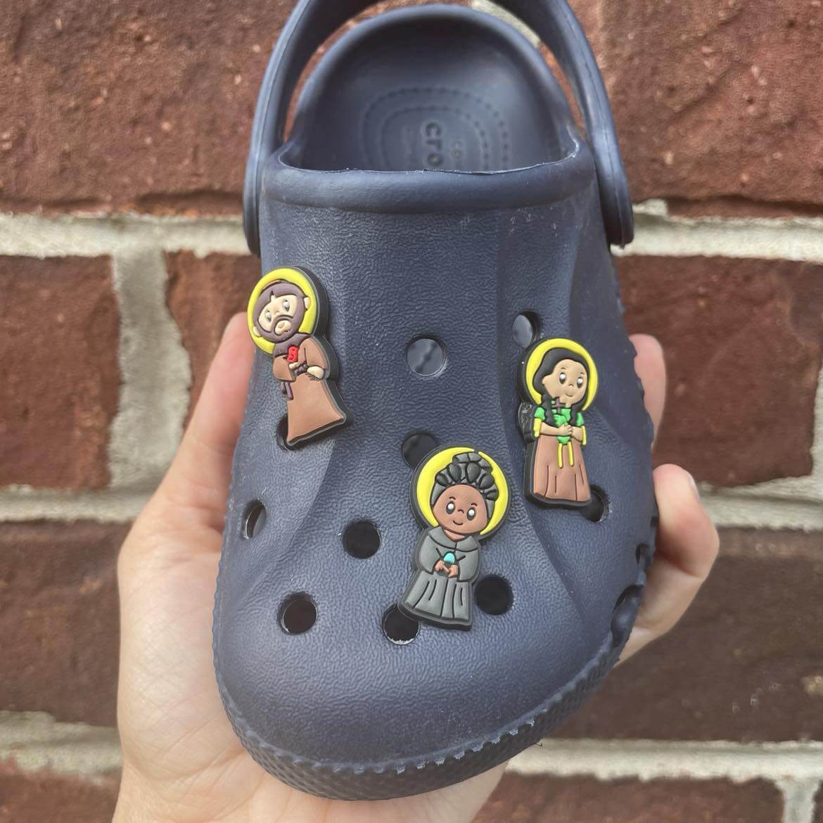 Blue Croc shoe adorned with Saint Friends silicone charms featuring iconic saints.