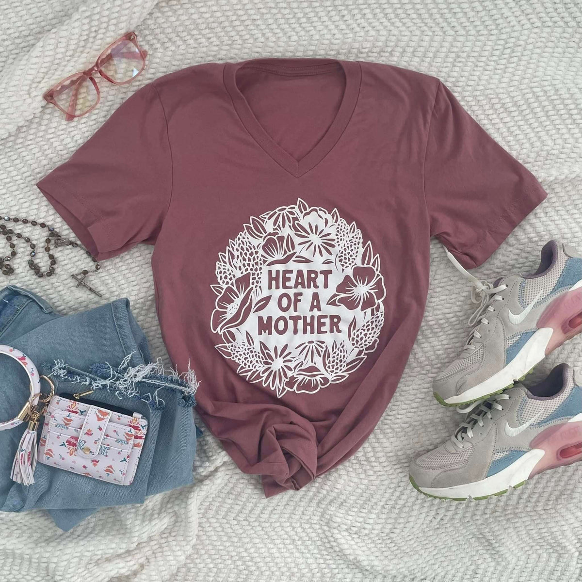 Maroon t-shirt with 'Heart of a Mother' floral design, styled with jeans, glasses, and sneakers. Ideal gift for moms.