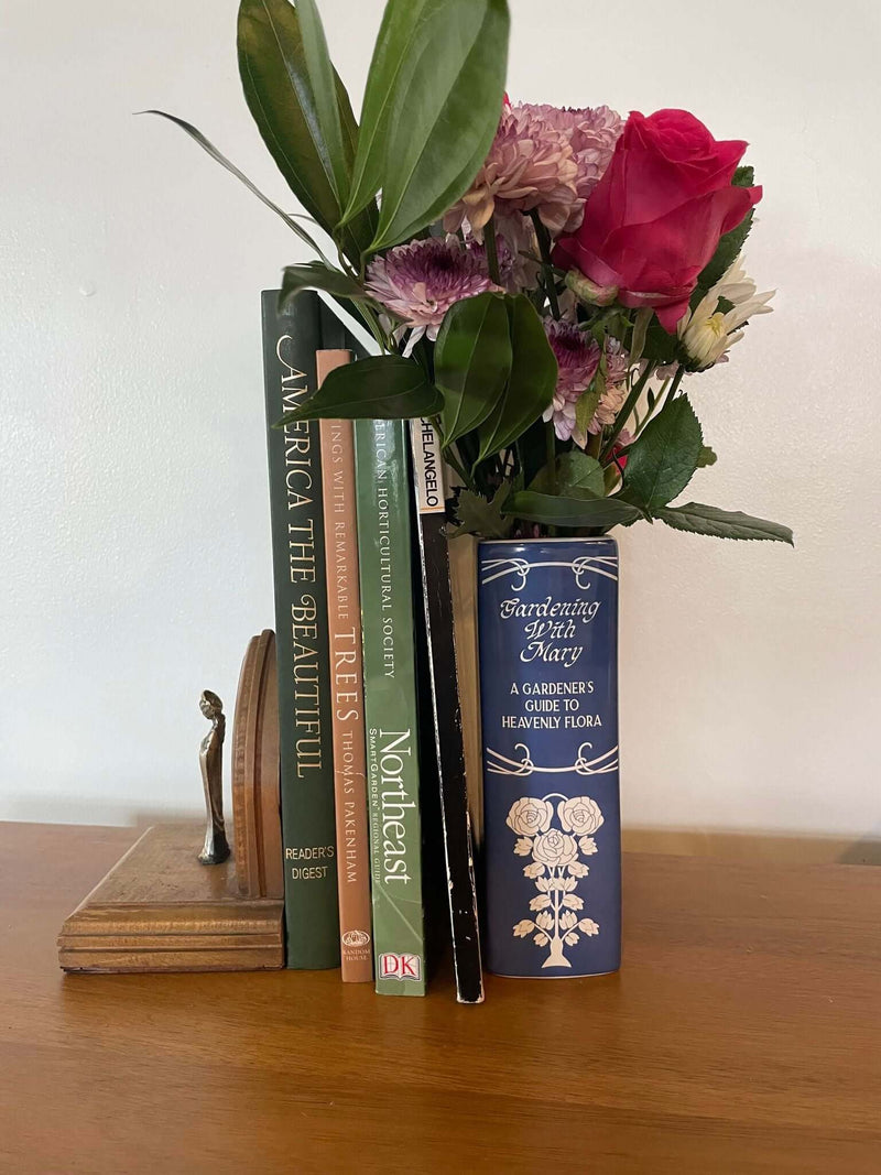 Ceramic book vase titled 'Gardening With Mary' with flowers, symbolizing spiritual growth through prayer and devotion.