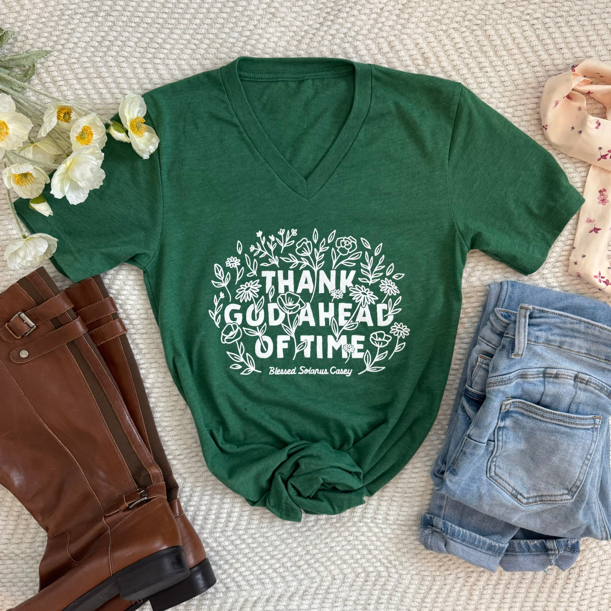 Green "Thank God Ahead of Time" tee inspired by Blessed Solanus Casey, promoting gratitude and faith, styled with boots and shorts.