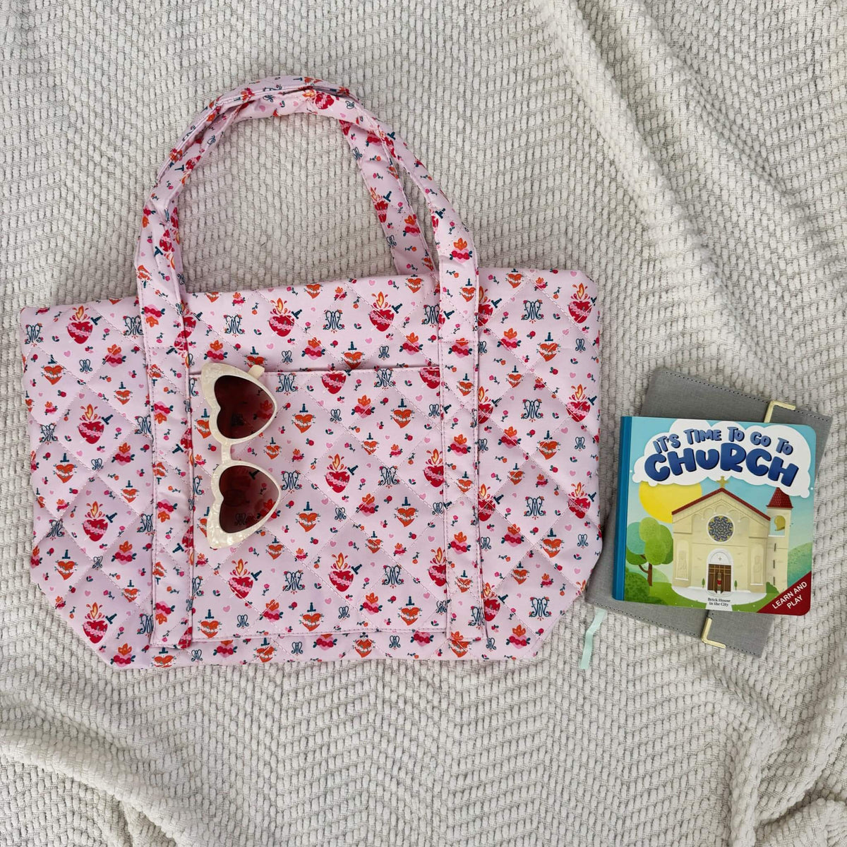 Auspice Maria Quilted Bag with heart sunglasses and a book on a textured fabric surface.