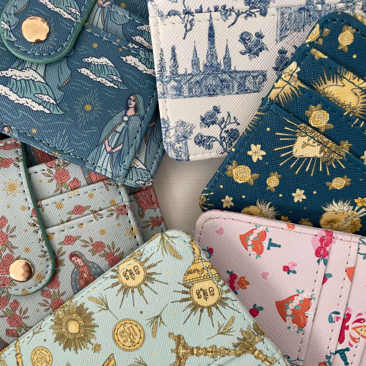 Collection of Catholic I.D. Wallets featuring Guadalupe, Stella, Lourdes, Holy Hearts, and Eucharistic patterns on faux leather.