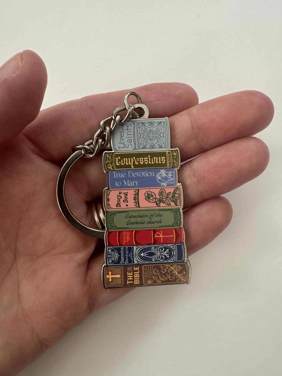 Hand holding a Catholic Library Book Stack Keychain featuring colorful miniature book replicas symbolizing devotion.