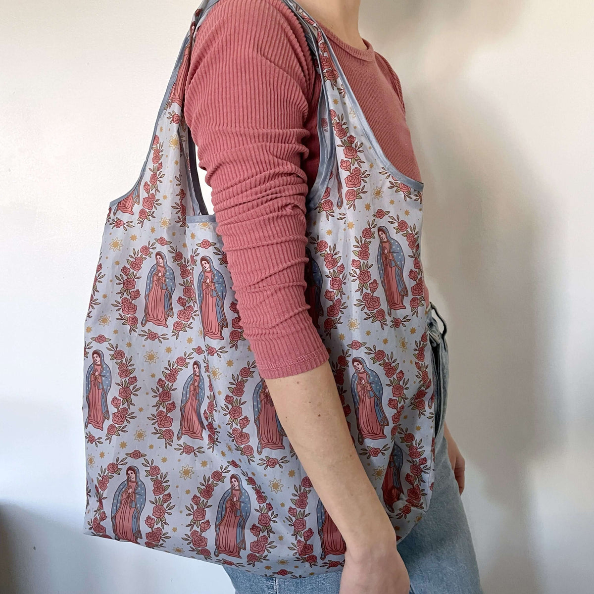 Woman carrying Catholic Reusable Grocery Bag from the Guadalupe Collection, featuring religious motif, eco-friendly design.