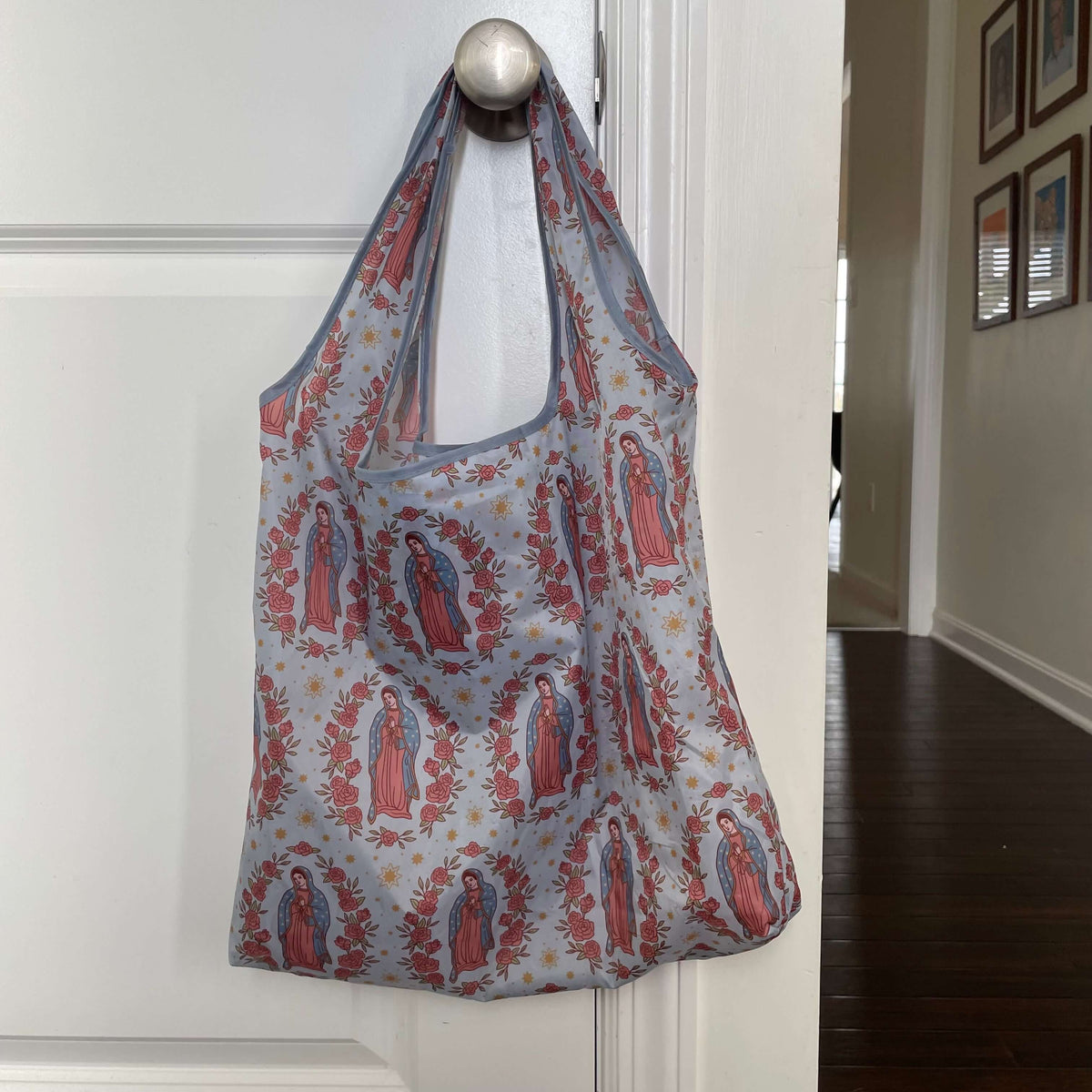 Guadalupe pattern Catholic reusable grocery bag hanging on door, eco-friendly 190T polyester bag for sustainable shopping.