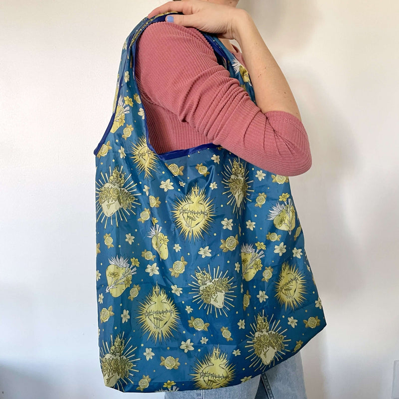 Woman holding Catholic Reusable Grocery Bag from Holy Hearts Collection with divine pattern, eco-friendly and stylish design.