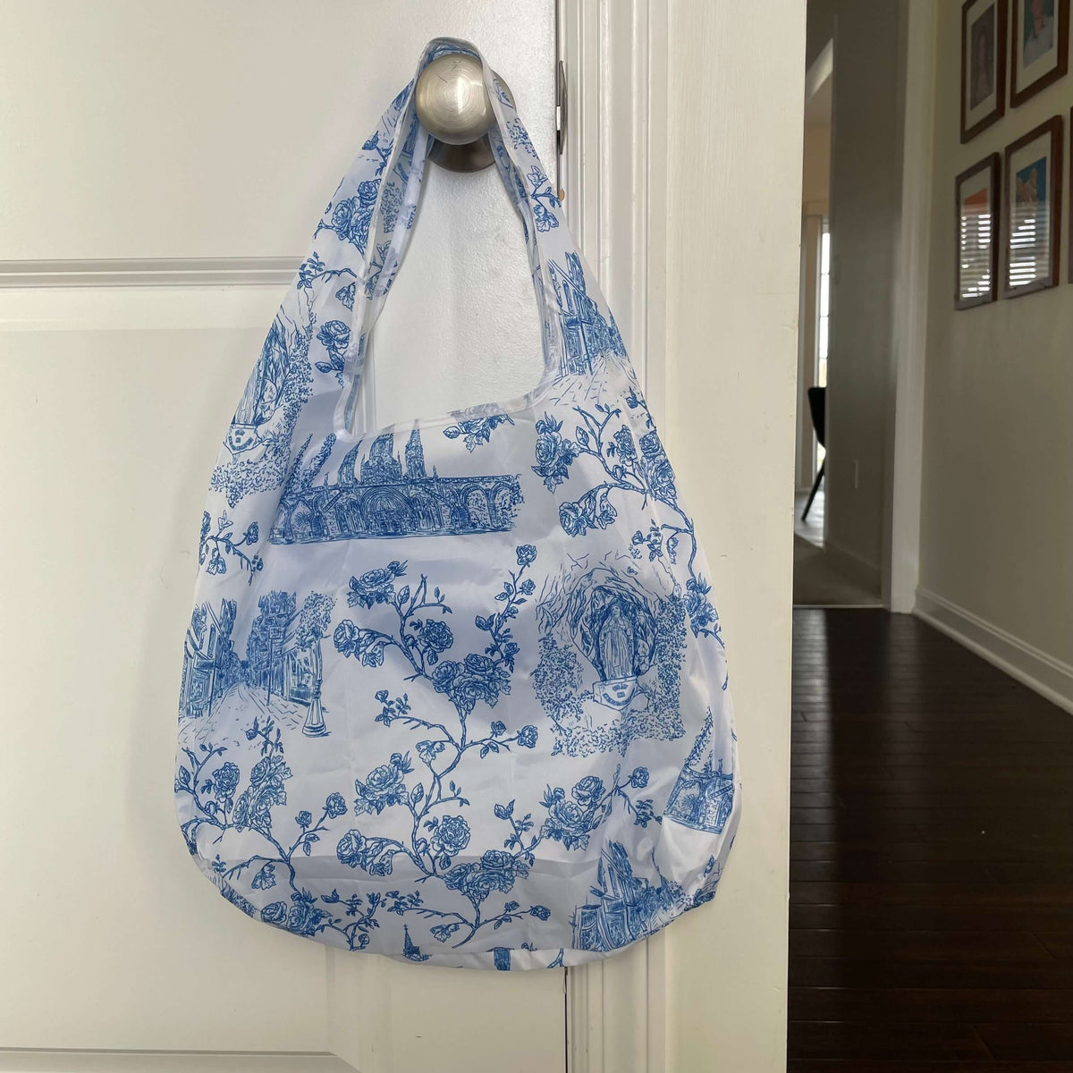 Catholic Lourdes reusable grocery bag with floral pattern hanging on white door
