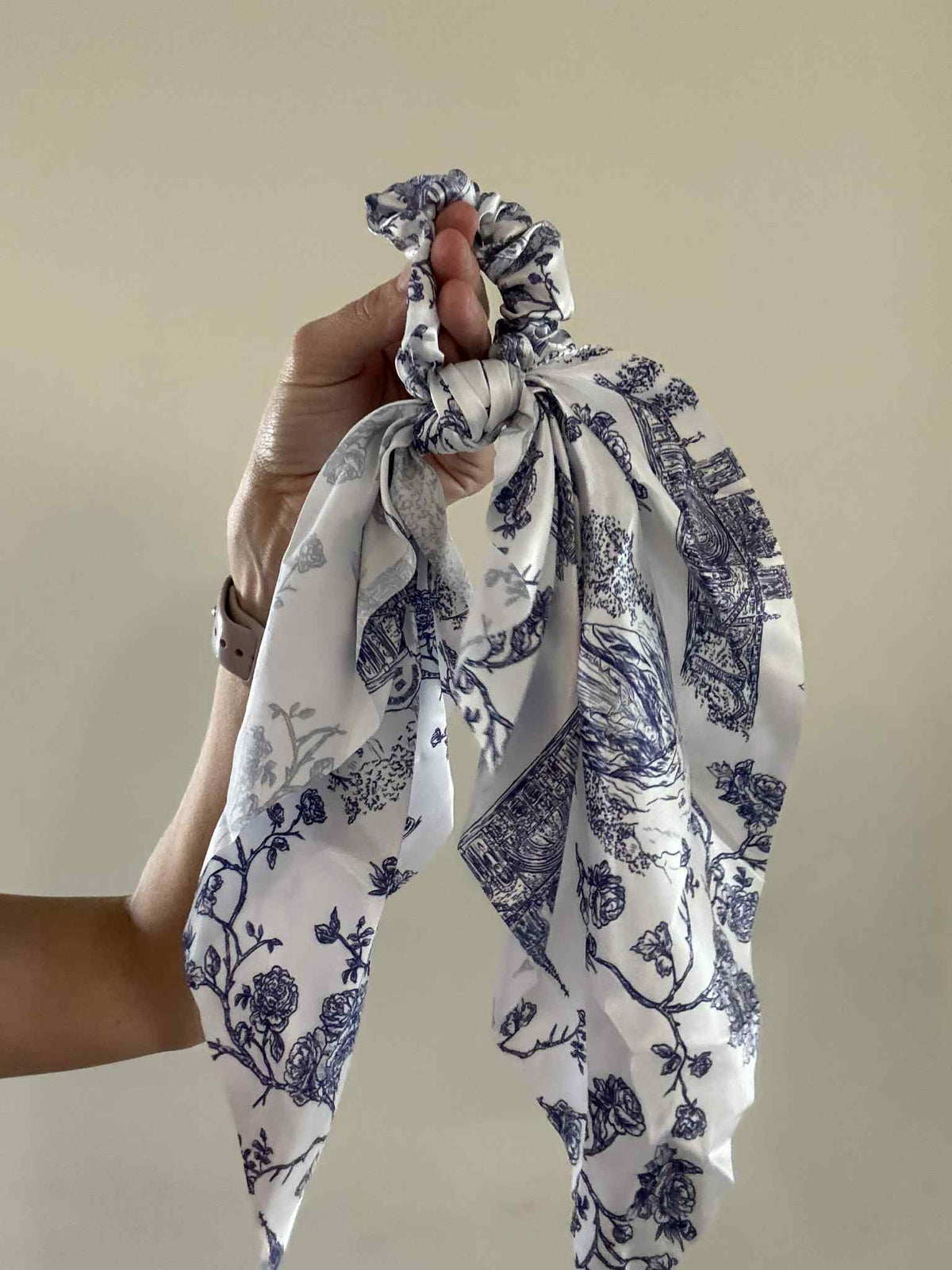 Hand holding a Catholic satin hanging scrunchie from the Lourdes Collection, featuring blue floral patterns on white fabric.