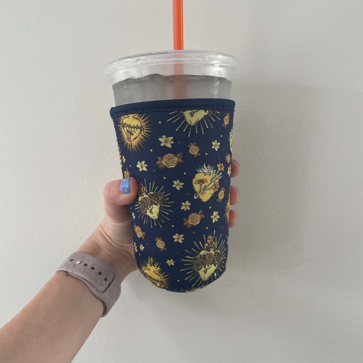 Hand holding a cup with a Catholic Cold Cup Sleeve featuring the Holy Hearts Collection design, neoprene material, keeping drink cold.