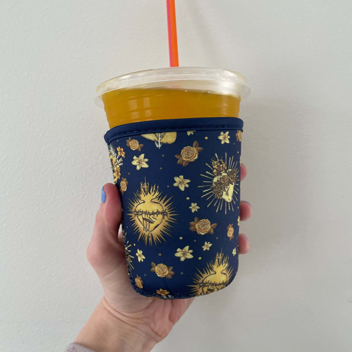 Hand holding a Catholic Cold Cup Sleeve from Holy Hearts Collection with floral and sacred heart design, fits coffee or tea.