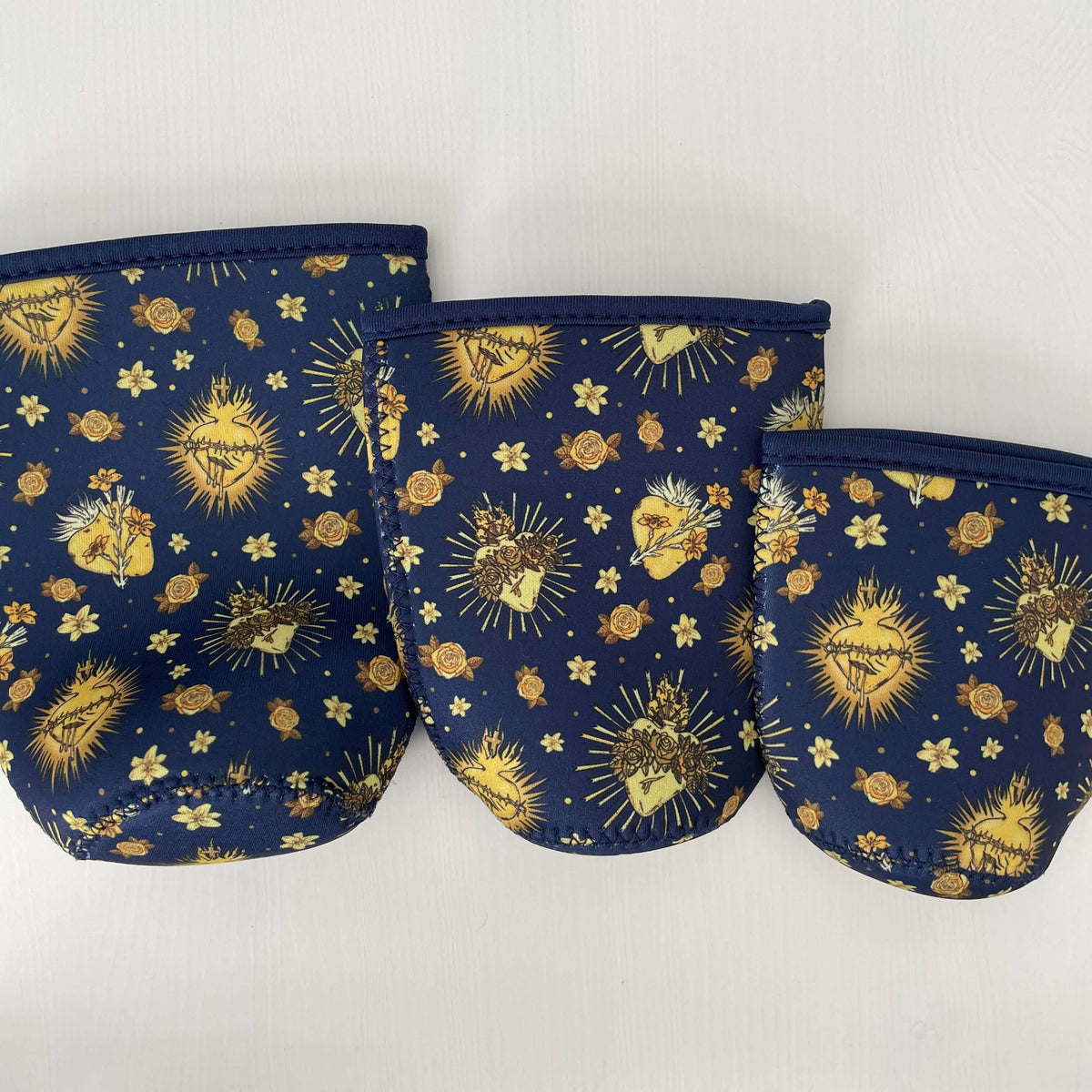 Three Catholic Cold Cup Sleeves from Holy Hearts Collection in different sizes with sacred heart design on blue background.