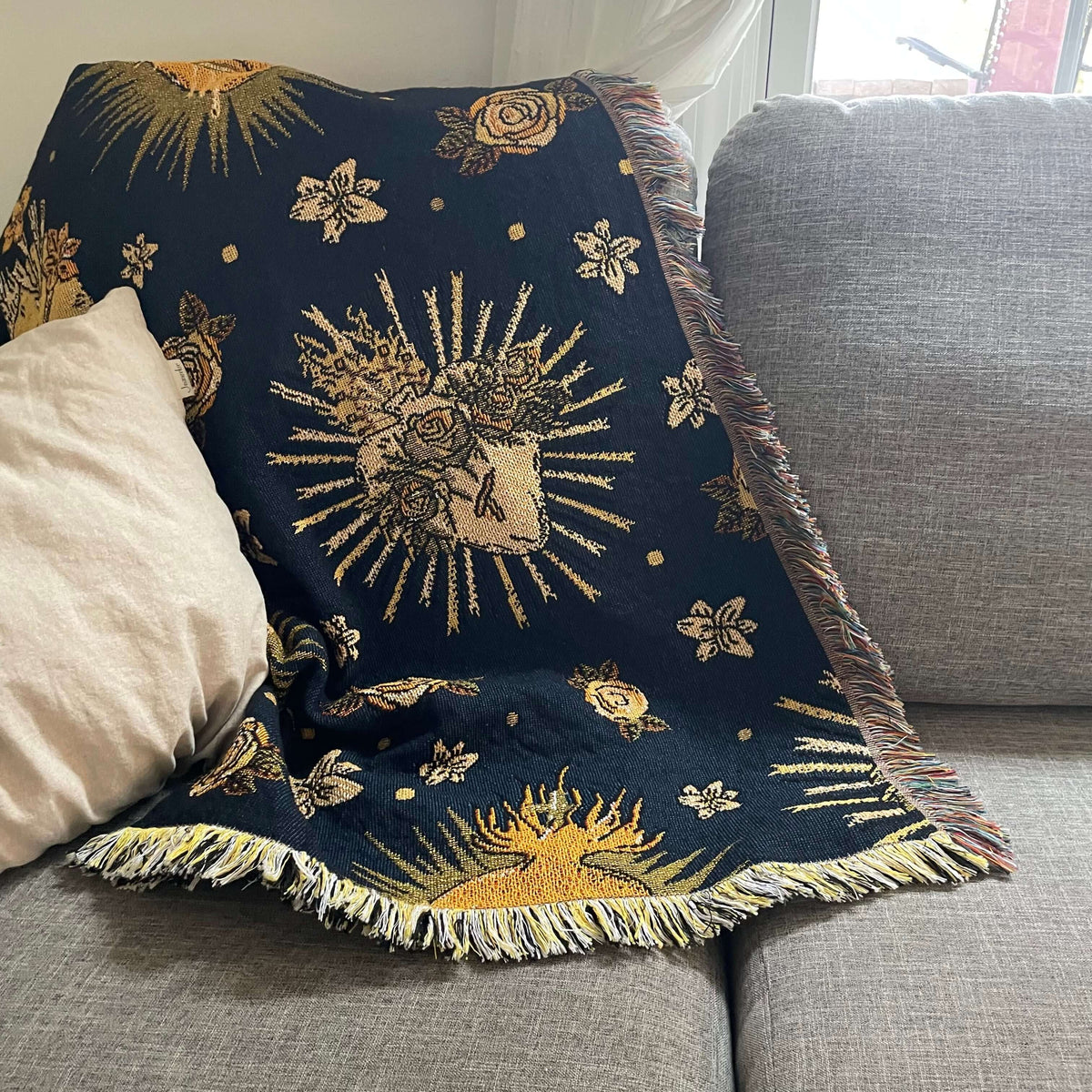Holy Hearts Woven Blanket on gray sofa, featuring Catholic motifs in woven cotton. Measures 51x63 inches for warmth and comfort.