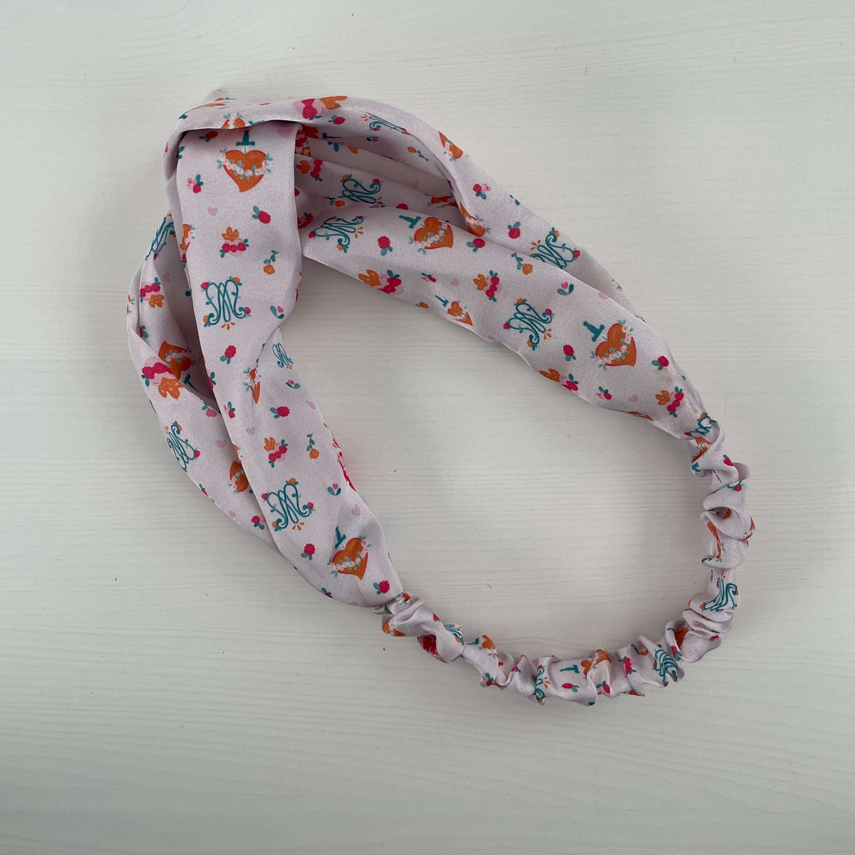 Auspice Maria patterned satin headband from the Catholic collection, featuring religious motifs and soft pink fabric.