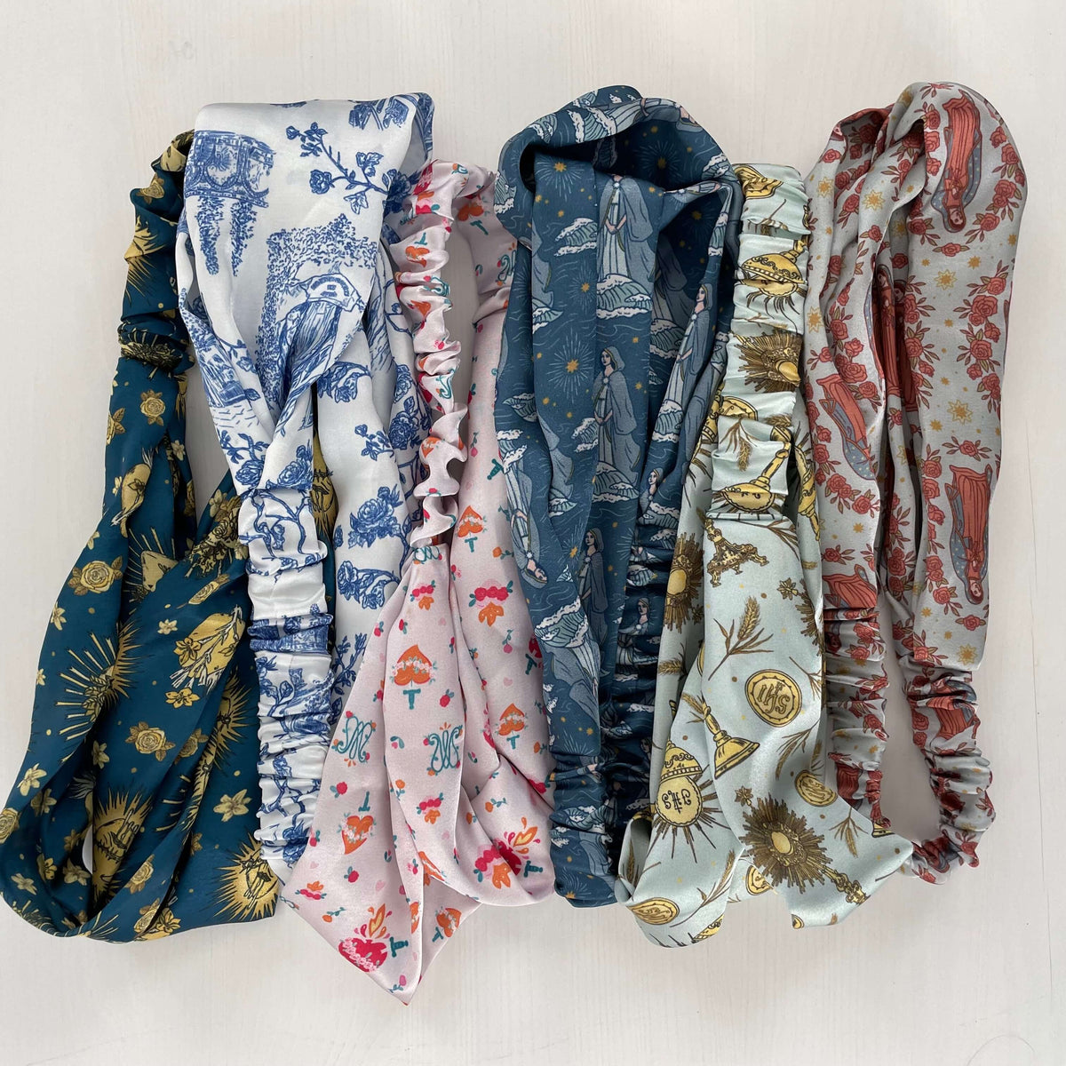 Collection of Catholic satin headbands from the Auspice Maria Collection featuring diverse divine patterns, blending faith and style.