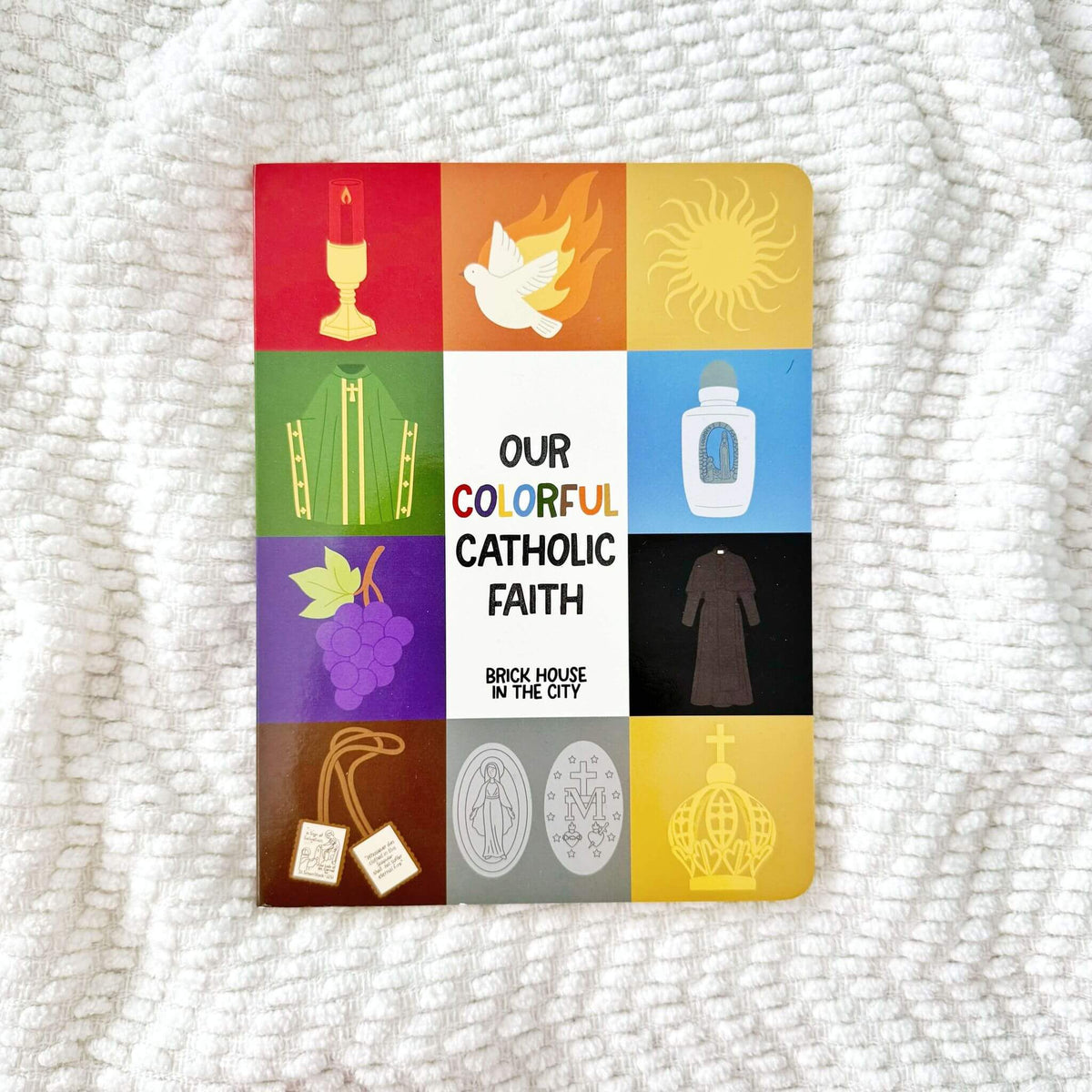Cover of 'Our Colorful Catholic Faith' children's book showcasing religious symbols and vibrant designs on a soft fabric background.
