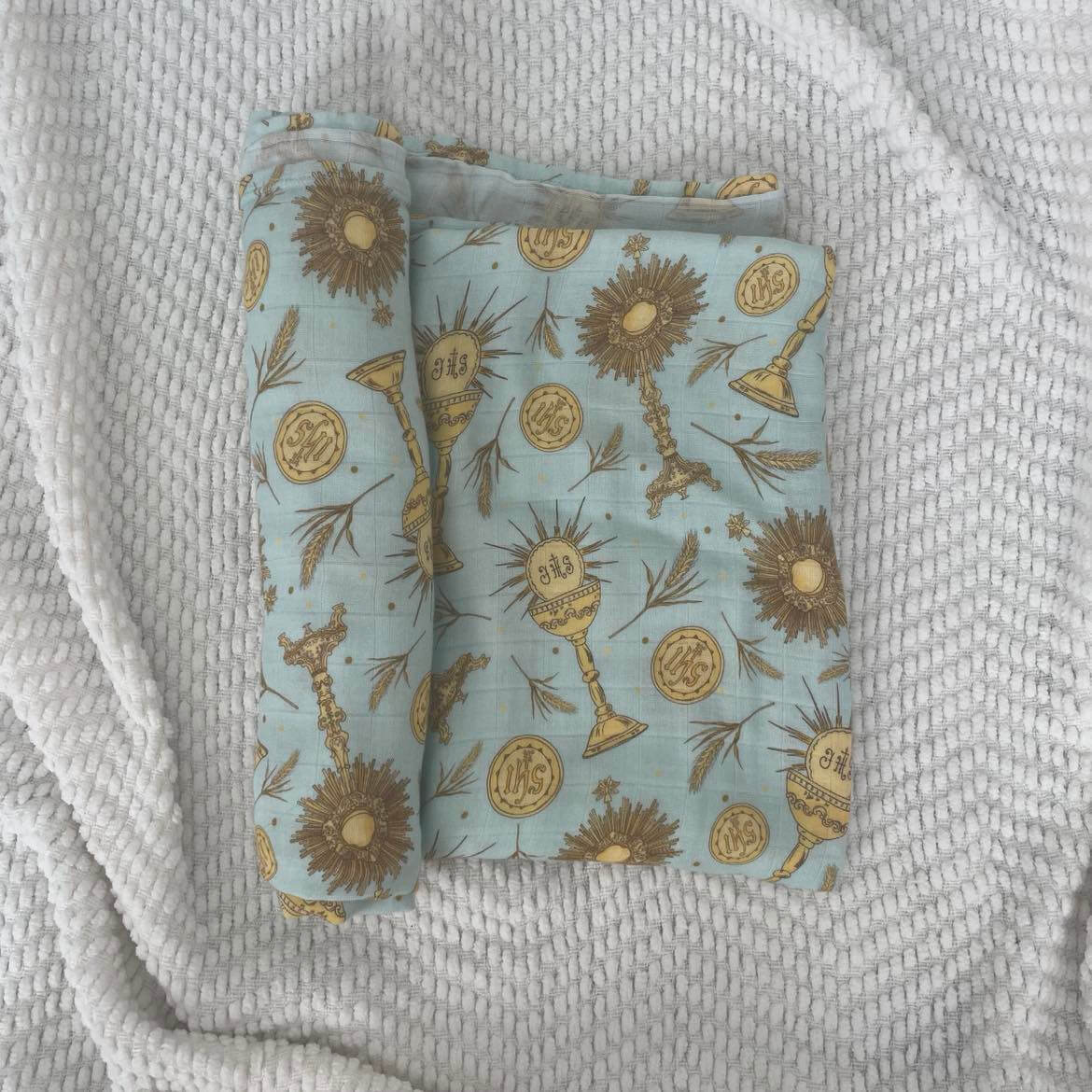Eucharistic swaddle blanket with religious motifs on a soft fabric, perfect for wrapping babies in comfort and faith.