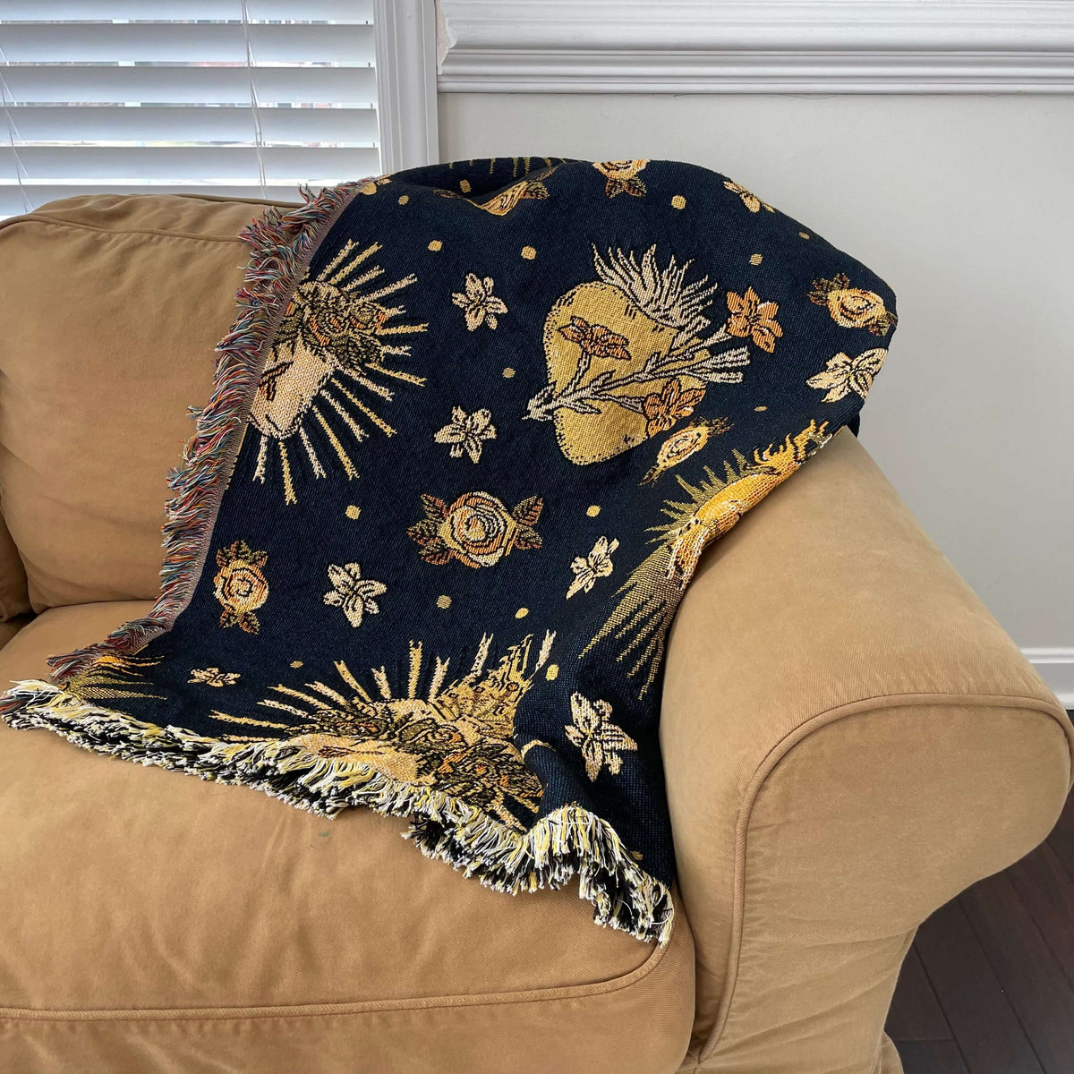 Holy Hearts Woven Blanket with Catholic design draped over beige sofa.