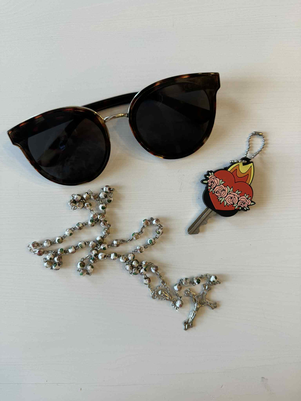 Alt Tag: Sunglasses, rosary, and Immaculate Heart key cap with floral design on a white background.