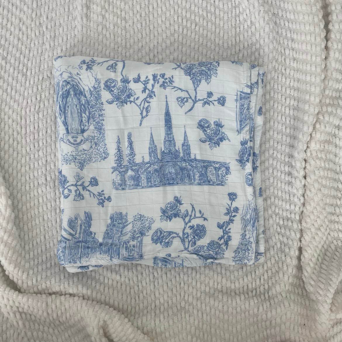 Lourdes Swaddle Blanket with blue religious patterns, crafted from organic bamboo cotton for baby's soft embrace, 47x47 inches.