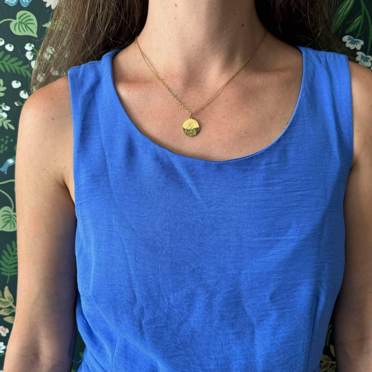 Woman wearing Madonna and Child necklace with 18k gold-plated pendant on an 18-inch chain, set against a floral background.