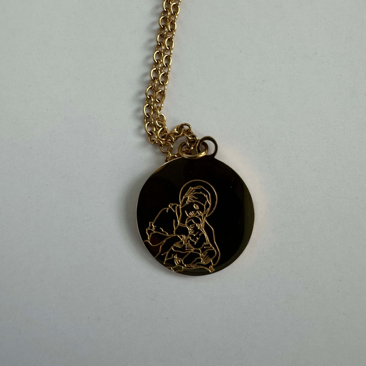 18k gold-plated Madonna and Child pendant necklace on white background. Elegantly depicts Mary and Jesus.