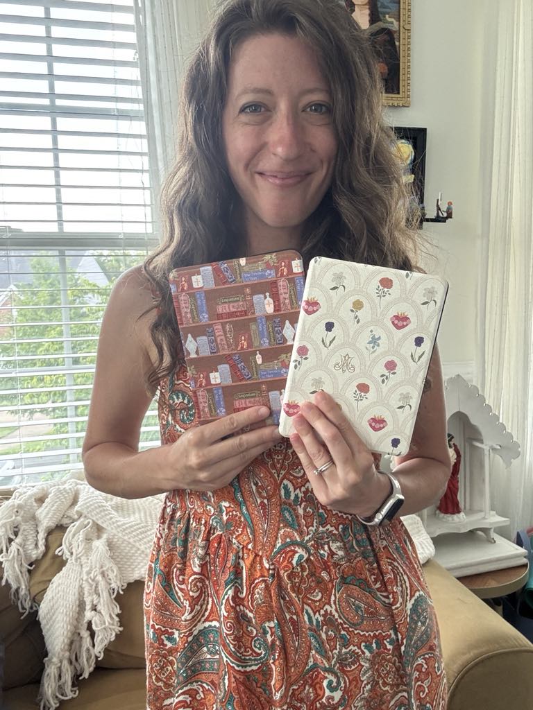 Woman holding Mary's Sacred Garden Kindle cases with floral designs in a living room setting.