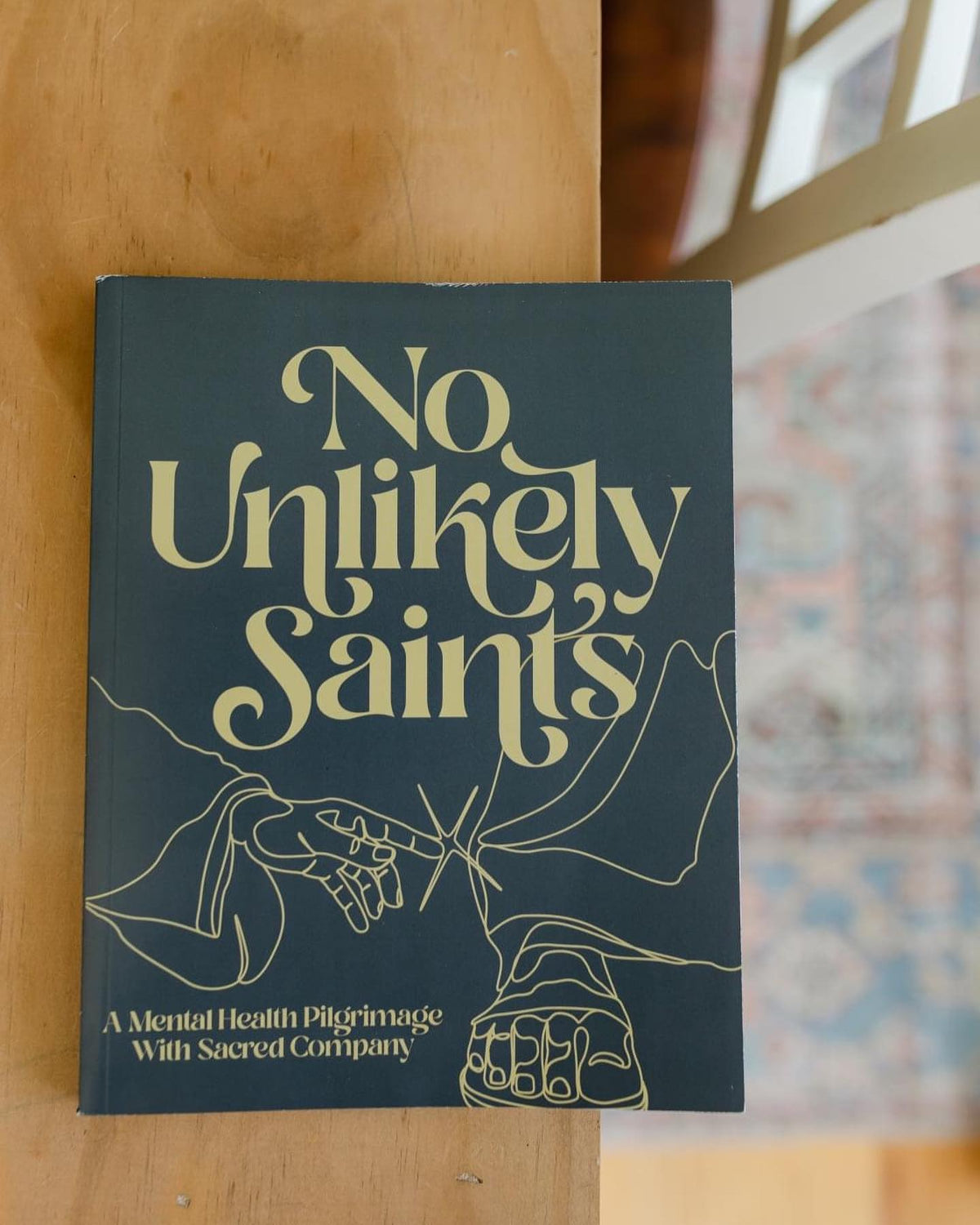 Book cover of 'No Unlikely Saints - A Mental Health Pilgrimage With Sacred Company' by Cameron Bellm, featuring a line art of hands and feet.