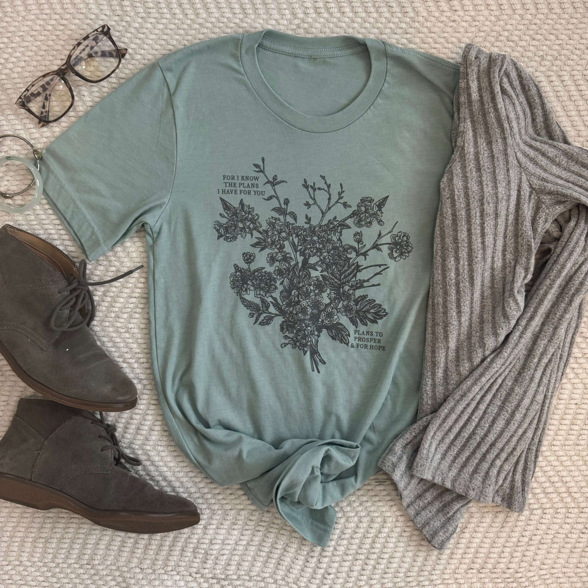 Plans to Prosper Jeremiah 29:11 tee with floral design next to glasses, boots, and a sweater on a beige background.