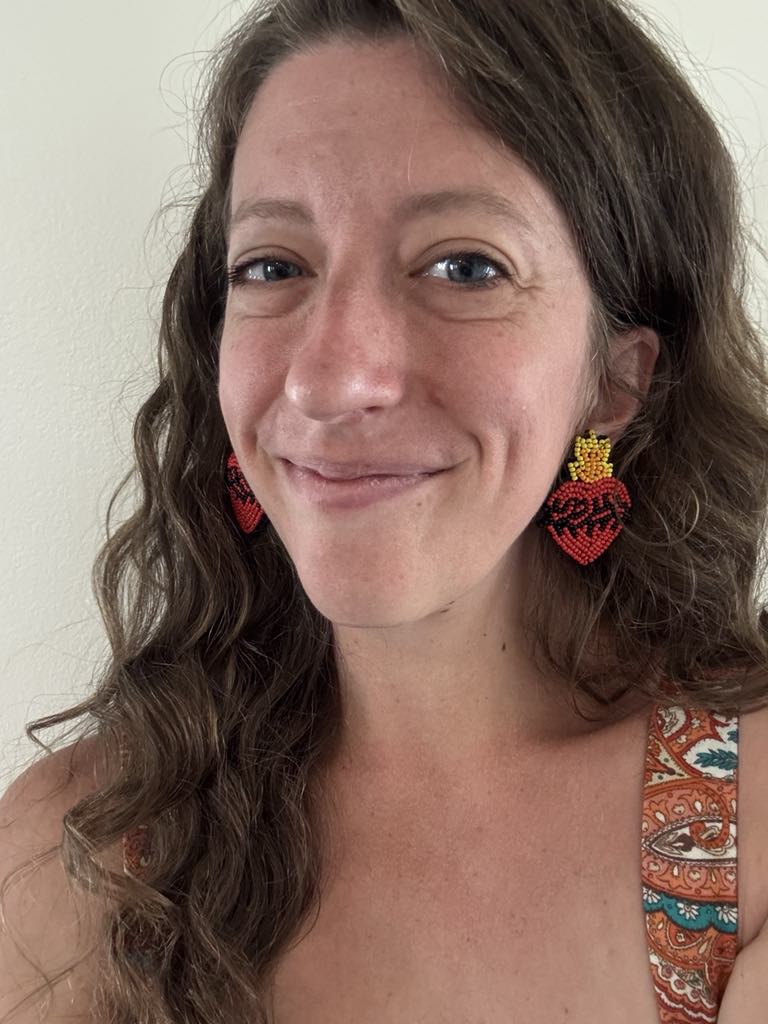 Woman wearing Sacred Heart beaded earrings with bold, joyful design. Handmade accessory symbolizing Christ's love. Shop now.