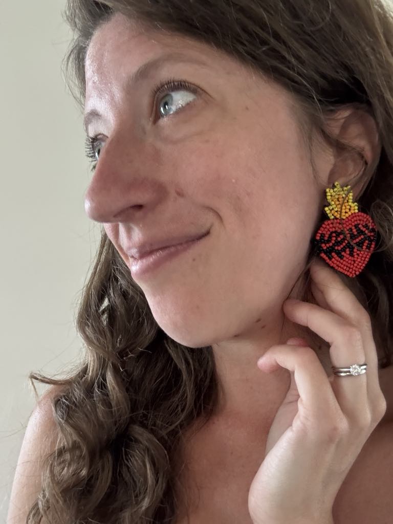 Woman wearing Sacred Heart beaded earrings, featuring vibrant red and yellow design, symbolizing devotion and love.