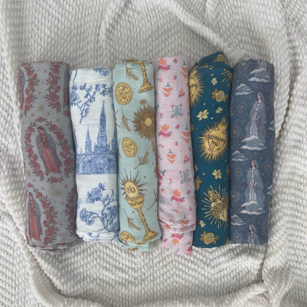 Stella Maris Swaddle Blanket collection with six Catholic-inspired designs in soft bamboo cotton on a woven background.