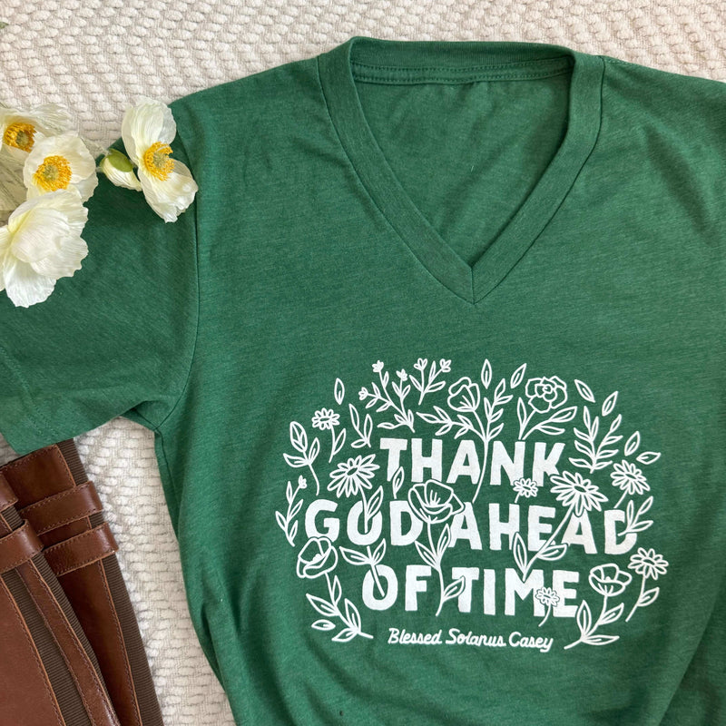 Green "Thank God Ahead of Time" tee inspired by Blessed Solanus Casey, featuring floral design and text on a soft background.