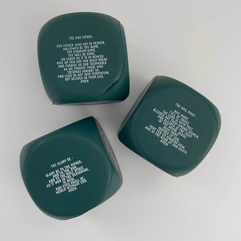 Three Catholic prayer cubes with inscriptions of "Our Father," "Hail Mary," and "Glory Be" prayers on a neutral background.