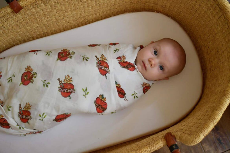 Baby swaddled in Holy Family Hearts blanket, featuring Sacred Heart of Jesus, Immaculate Heart of Mary, and Chaste Heart of Saint Joseph design.