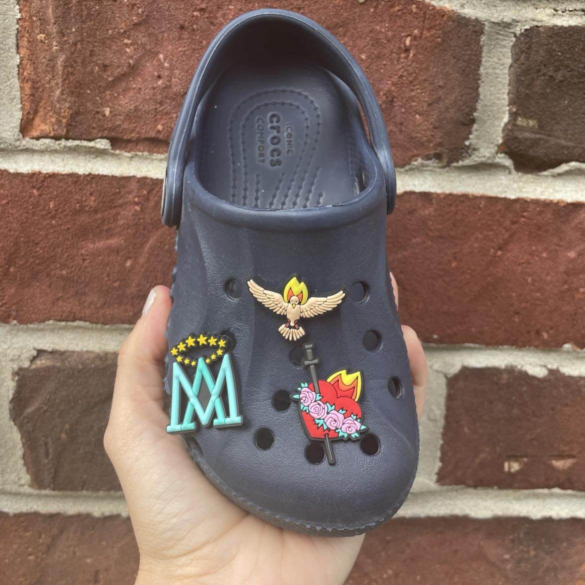 Dark blue Croc shoe adorned with Catholic-themed silicone charms including Holy Spirit Dove and Immaculate Heart of Mary.