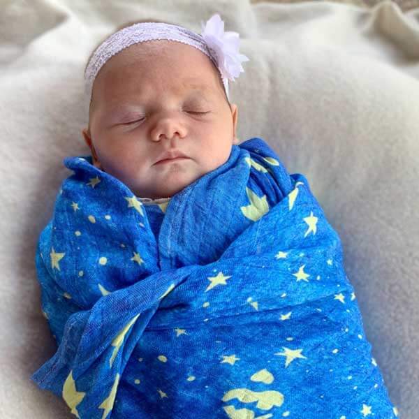 Baby peacefully sleeping wrapped in Mary's Mantle Swaddle, featuring a blue starry design, symbolizing comfort and protection.
