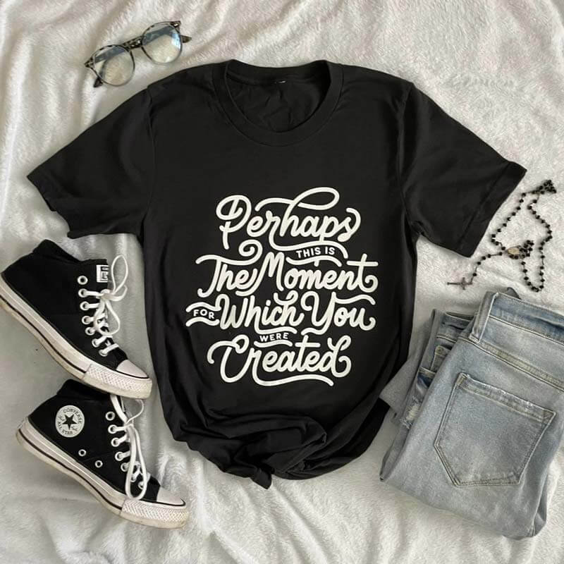 Black t-shirt with 'Perhaps This Is The Moment For Which You Were Created' text, laid with jeans, sneakers, and accessories.