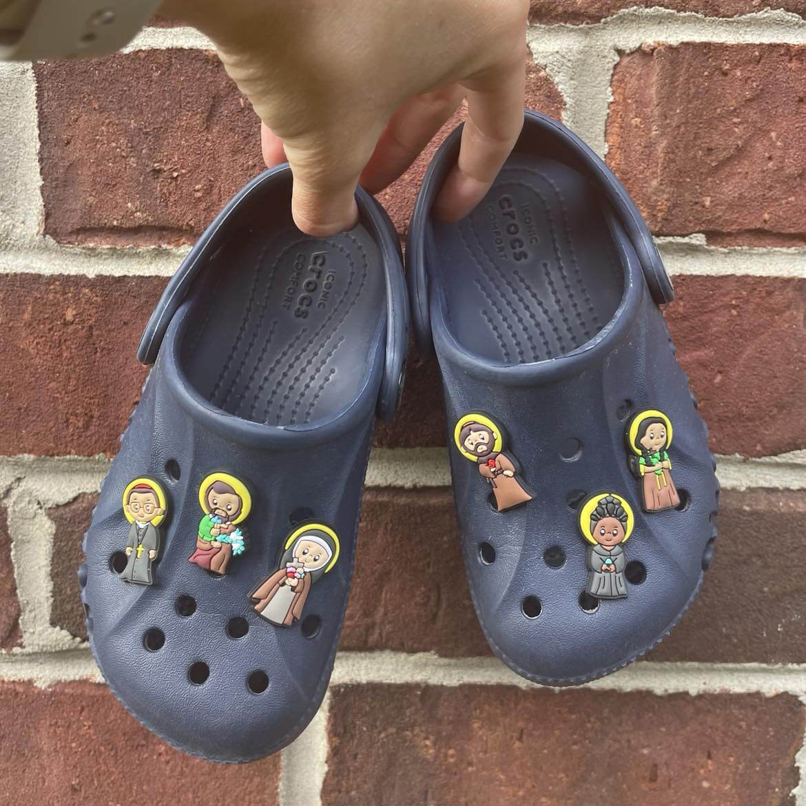 Saint Friends Croc Charm Set featuring saints Joseph, Francis, Oscar Romero, Josephine Bakhita, Kateri Tekakwitha on blue Crocs.