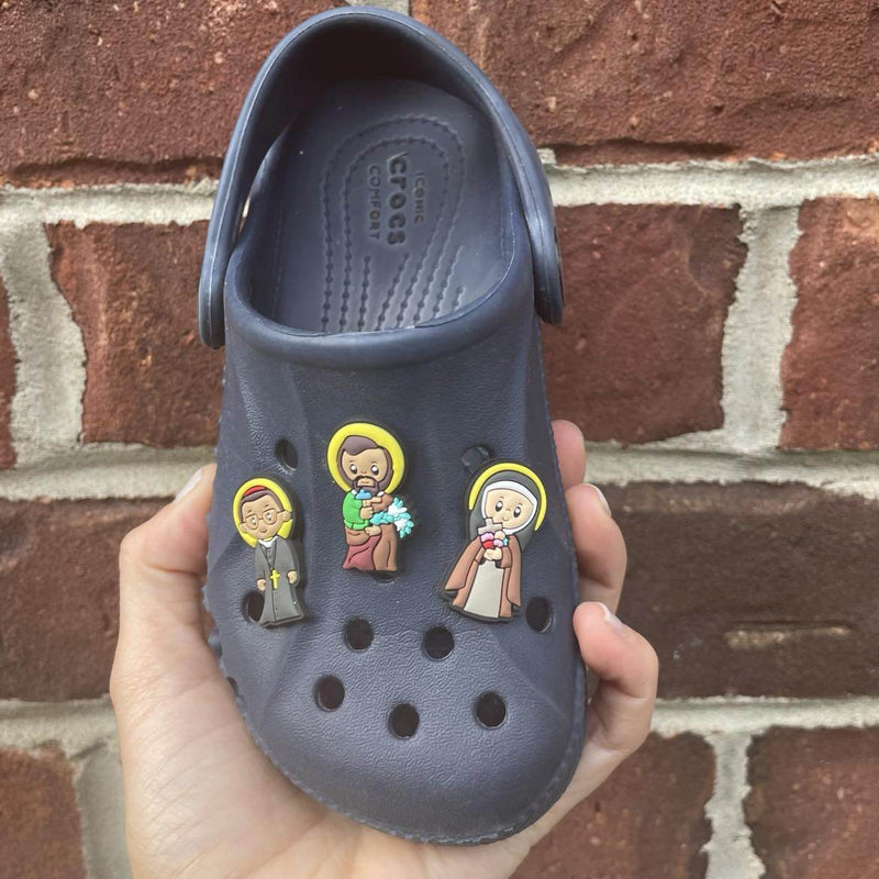Saint Friends Croc Charm Set featuring Saint Joseph, Saint Francis, and Saint Josephine Bakhita on a black Croc shoe.