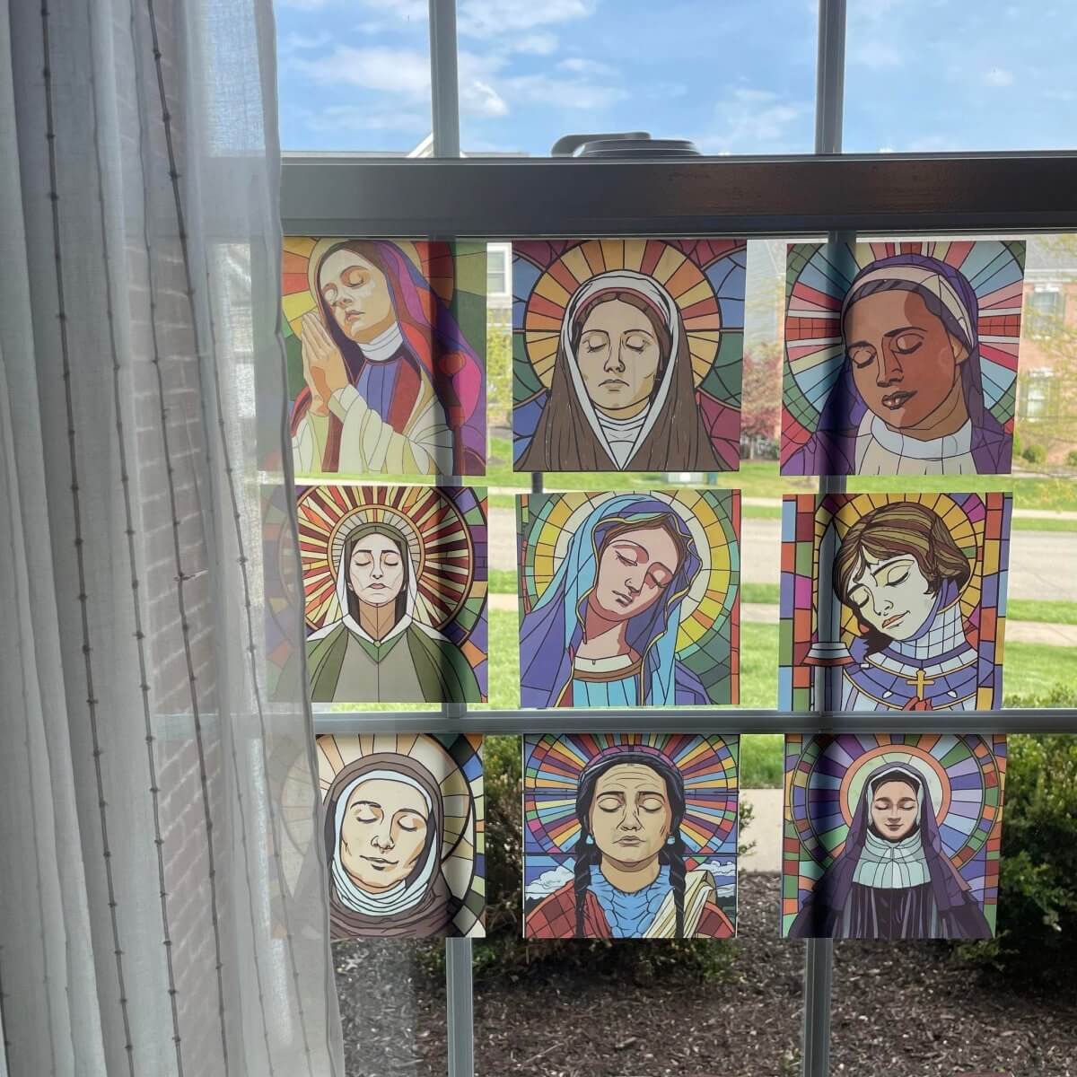 Stained glass window clings depicting nine beloved saints displayed on a window. Ideal for home decor and religious inspiration.